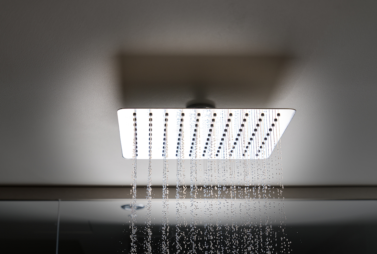 Water flows from the tropical shower. Large water consumption. Chrome large shower head, modern design. Water flowing from the square shower head in a modern bathroom.